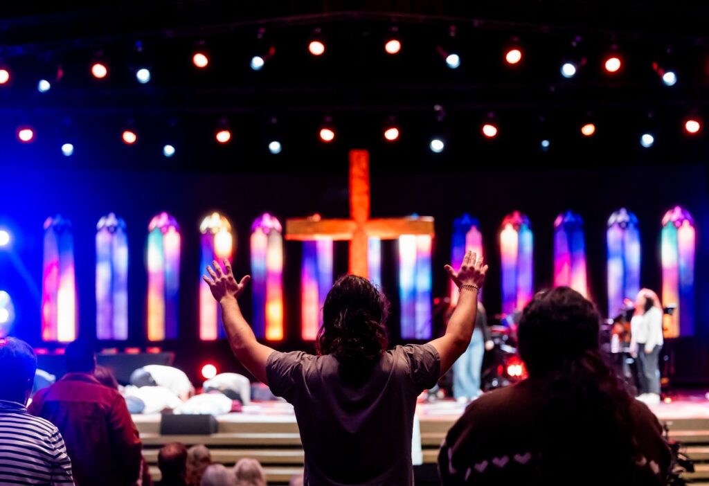 Lively church service with congregation worshipping under colorful stained-glass lighting.