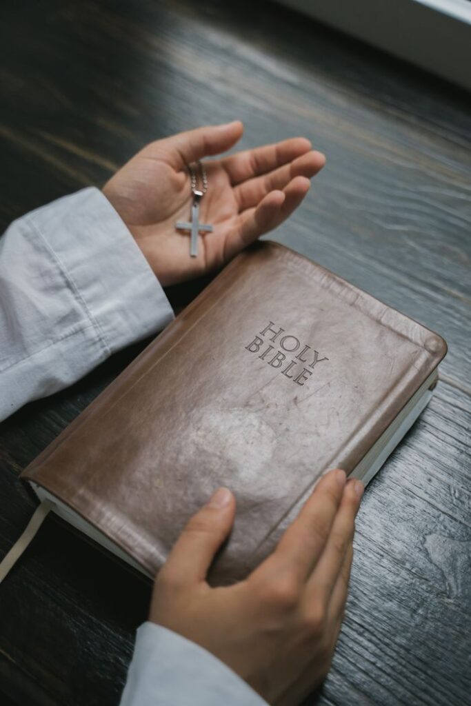 Close-up of hands holding a Holy Bible with a cross necklace, symbolizing faith and spirituality.